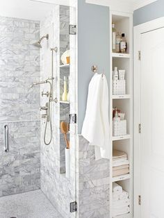 a walk in shower sitting next to a white door and shelves filled with towels on the wall