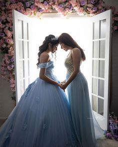 two women in blue dresses standing next to each other near an open door with flowers on it