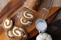 cinnamon roll with icing on a cutting board next to pumpkins and powdered sugar