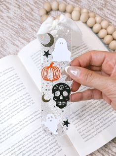 a person is holding up a bookmark with skulls and pumpkins on it in front of an open book