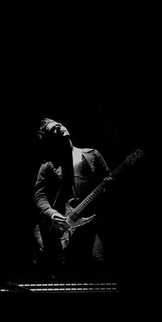 a black and white photo of a man playing an electric guitar in front of a dark background