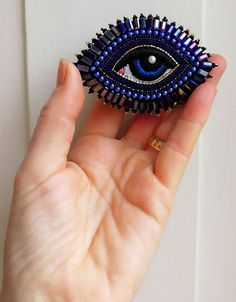 a hand holding a blue beaded evil eye brooch