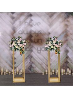 two tall gold vases with flowers on each one stand in front of a backdrop