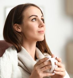 a woman sitting in a chair holding a cup and looking up into the sky with her eyes closed