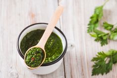 a wooden spoon sitting in a cup filled with green pesto next to parsley