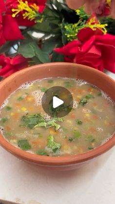 a bowl filled with soup sitting on top of a table next to red flowers and a knife