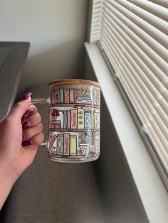 a hand holding a coffee mug with books on the front and back sides, in front of a window