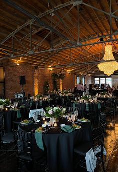 a large room with tables and chairs covered in black linens, green tablecloths and lights hanging from the ceiling