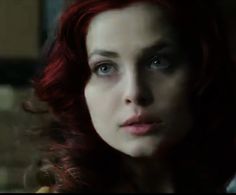 a woman with red hair and blue eyes looks at the camera while she stares into the distance