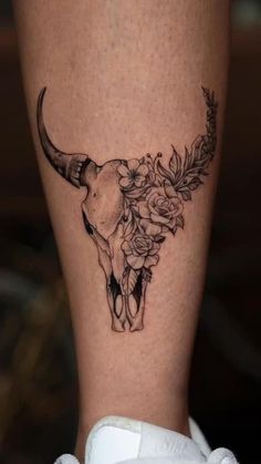 a tattoo on the leg of a woman with flowers and a bull's skull