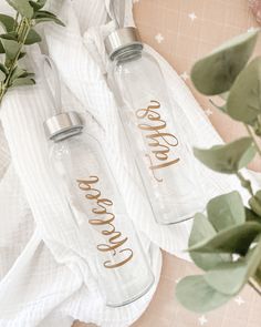 two personalized glass water bottles sitting on top of a towel next to eucalyptus leaves