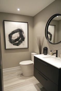 a white toilet sitting next to a bathroom sink under a mirror and a painting on the wall