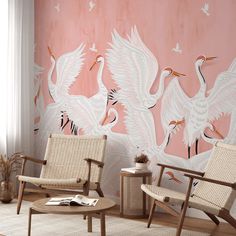 two chairs and a table in front of a pink wall with white cranes on it