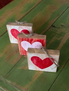 three small boxes with hearts painted on them are sitting on a wooden table and tied to twine