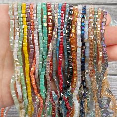 there are many different colored beads on the hand that is holding it up to be used as bracelets or necklaces