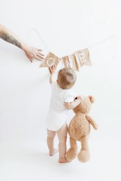 a baby standing next to a teddy bear