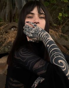 a woman with black and white tattoos on her arm holding her hands up to her face