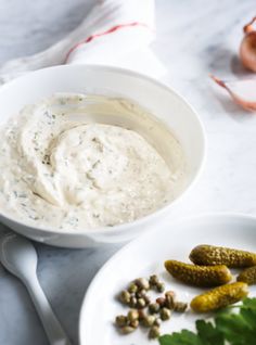 a white bowl filled with dip next to some pickles and corian seeds on a plate