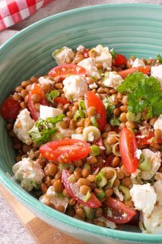 a green bowl filled with lots of food on top of a wooden cutting board next to a red and white checkered table cloth