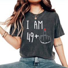 a woman wearing a black shirt with the words i am 47 plus on it and a red lipstick in her hand