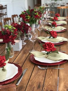 the table is set with red roses and place settings