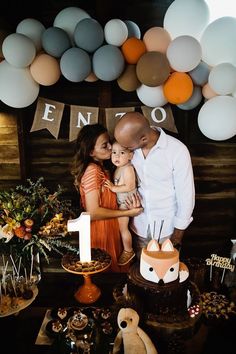 a man and woman holding a baby in front of a cake