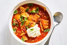 a white bowl filled with pasta, meat and cheese on top of a table next to a spoon