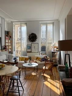 a living room filled with lots of furniture next to tall windows and bookshelves