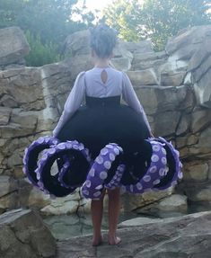 a woman is standing on some rocks with an octopus ring around her neck and purple polka dots