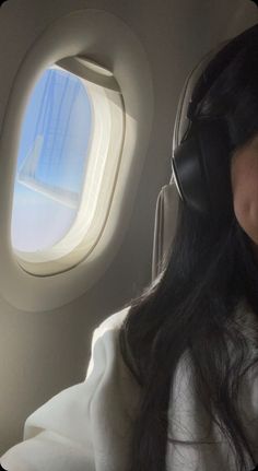 a woman wearing headphones sitting in an airplane looking out the window at the sky