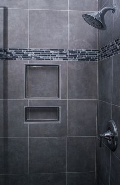 a walk in shower sitting next to a tiled wall and floor covered in gray tiles