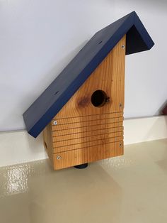 a wooden birdhouse with a blue roof on the floor in front of a white wall