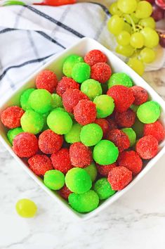 a white bowl filled with green and red gummy bears next to grapes on a marble counter