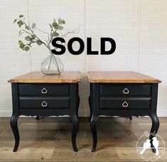 two black nightstands with wooden top and one has a vase on it for sale