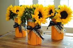 three vases with sunflowers tied in black ribbon on a wooden table next to a window