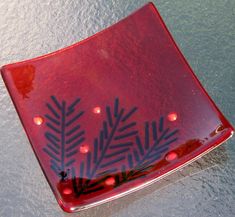 a red plate with black designs on it sitting on top of a table next to water