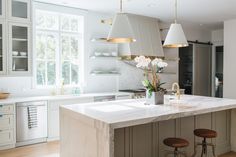 a large kitchen with white cabinets and marble counter tops, two pendant lights over the island