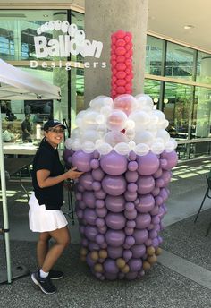 a woman standing next to a giant purple and white balloon sculpture in front of a building