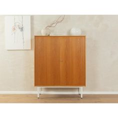 a wooden cabinet sitting on top of a hard wood floor next to a painting and vase