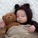 a baby in a bear costume is holding a teddy bear