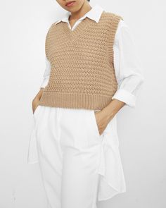 a woman in white pants and a beige knitted sweater is standing with her hands on her hips