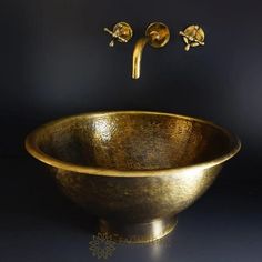 a gold sink with two faucets on the wall next to it and a black background