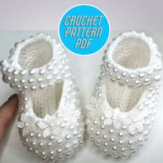 a hand holding a pair of white baby shoes with pearls on the toes and bottom