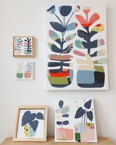 three framed art pieces on a wall above a wooden table with two vases and one plant