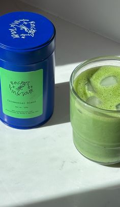 a green drink in a glass next to a blue container on a white countertop