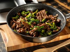 beef and broccoli in a skillet on a wooden cutting board with tongs