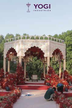 two people kneeling on the ground in front of a gazebo surrounded by red flowers