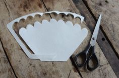 a pair of scissors sitting on top of a wooden table next to cut out paper