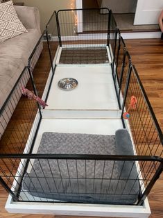 a dog crate is sitting on the floor in front of a gray couch and grey rug