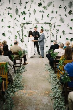 a bride and groom standing at the end of their wedding ceremony with greenery on the wall behind them